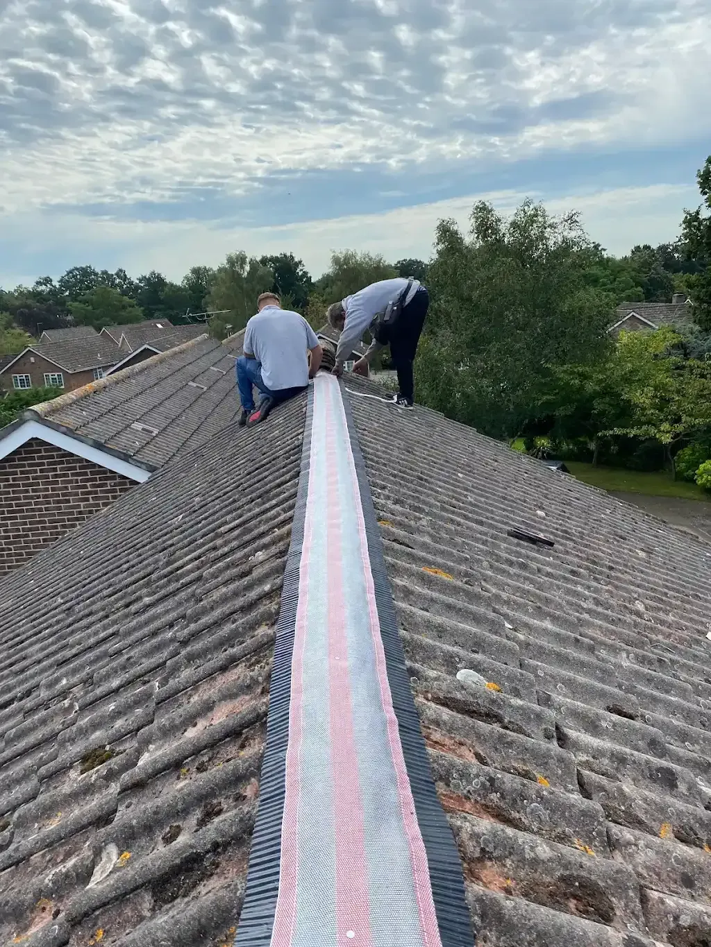 Two roofers installing a ridge system on a tiled house roof.